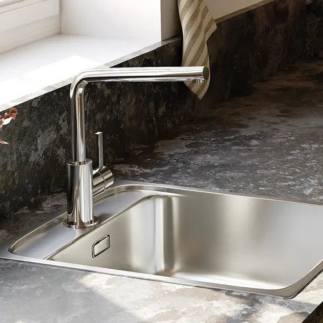 Nahaufnahme einer modernen Einbau Spüle aus Edelstahl mit geradliniger Mischbatterie in einer Küche mit dunkler Stein Arbeitsplatte und Fensterbank, ideal für zeitgemäße Küchenplanung.